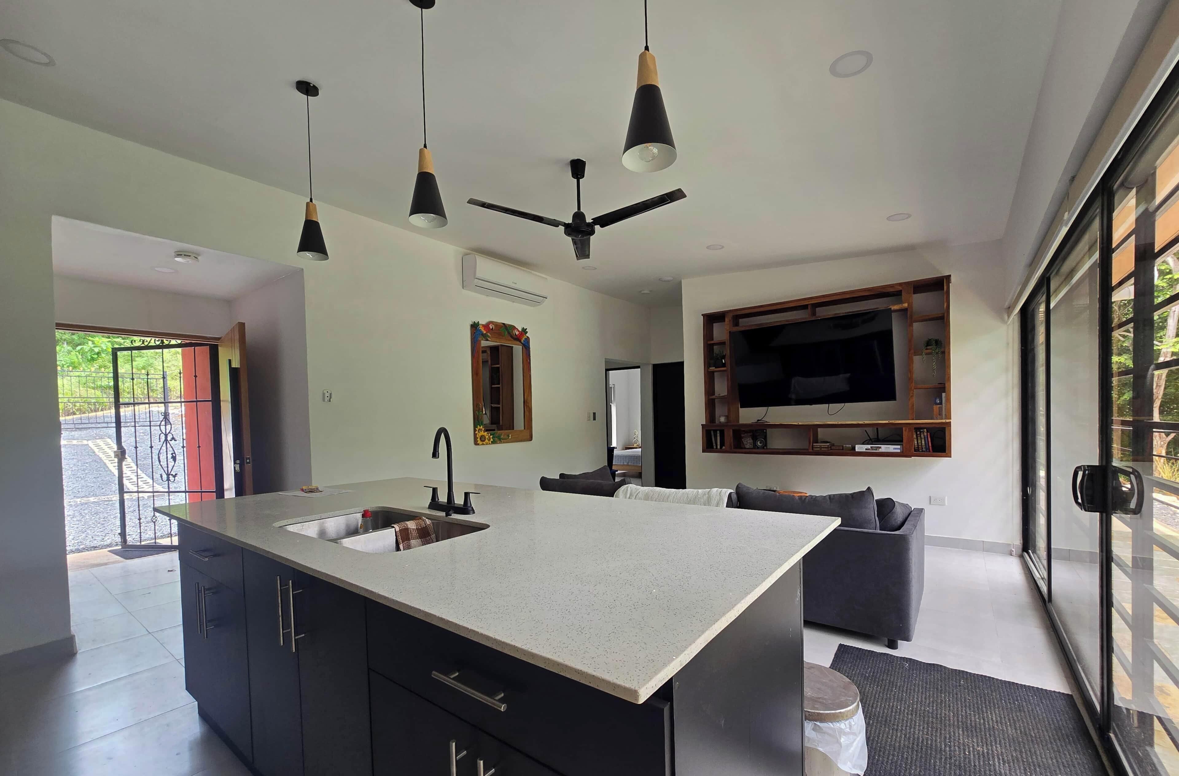 Una cocina moderna con una isla central, un área de comedor con un sofá y un televisor grande montado en la pared.