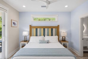 A bedroom with a bed, two bedside tables with lamps, a ceiling fan, a window with a view, and a framed artwork on the wall. - New 4BR Ground-Level Home  Pool  Near Beach (Saint George Island)