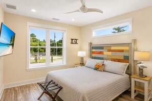 Une chambre à coucher comprenant un lit, deux tables de chevet, un ventilateur de plafond et une fenêtre donnant sur un paysage verdoyant.