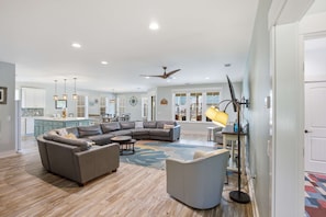 A spacious living room with a large L-shaped sectional sofa, a round coffee table, and a modern floor lamp. - New 4BR Ground-Level Home  Pool  Near Beach (Saint George Island)