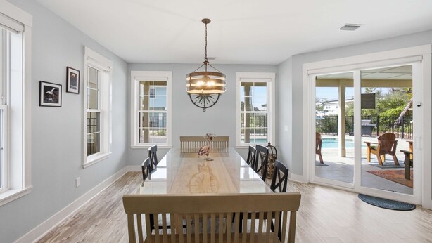 A spacious dining area with a long table, chairs, and a hanging light fixture. - New 4BR Ground-Level Home | Pool | Near Beach (Saint George Island)