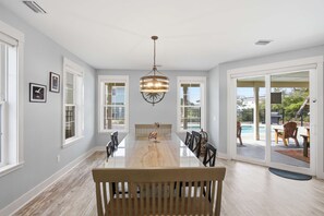A spacious dining area with a long table, chairs, and a hanging light fixture. - New 4BR Ground-Level Home  Pool  Near Beach (Saint George Island)
