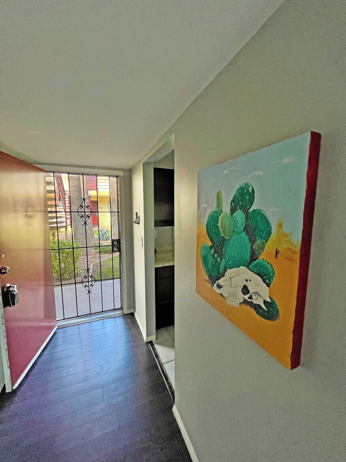 Ein Korridor mit einem Bild von einem Kaktus und einem Koala, einer Tür mit rotem Rahmen und einer Treppe, die in einen Außenbereich führt.