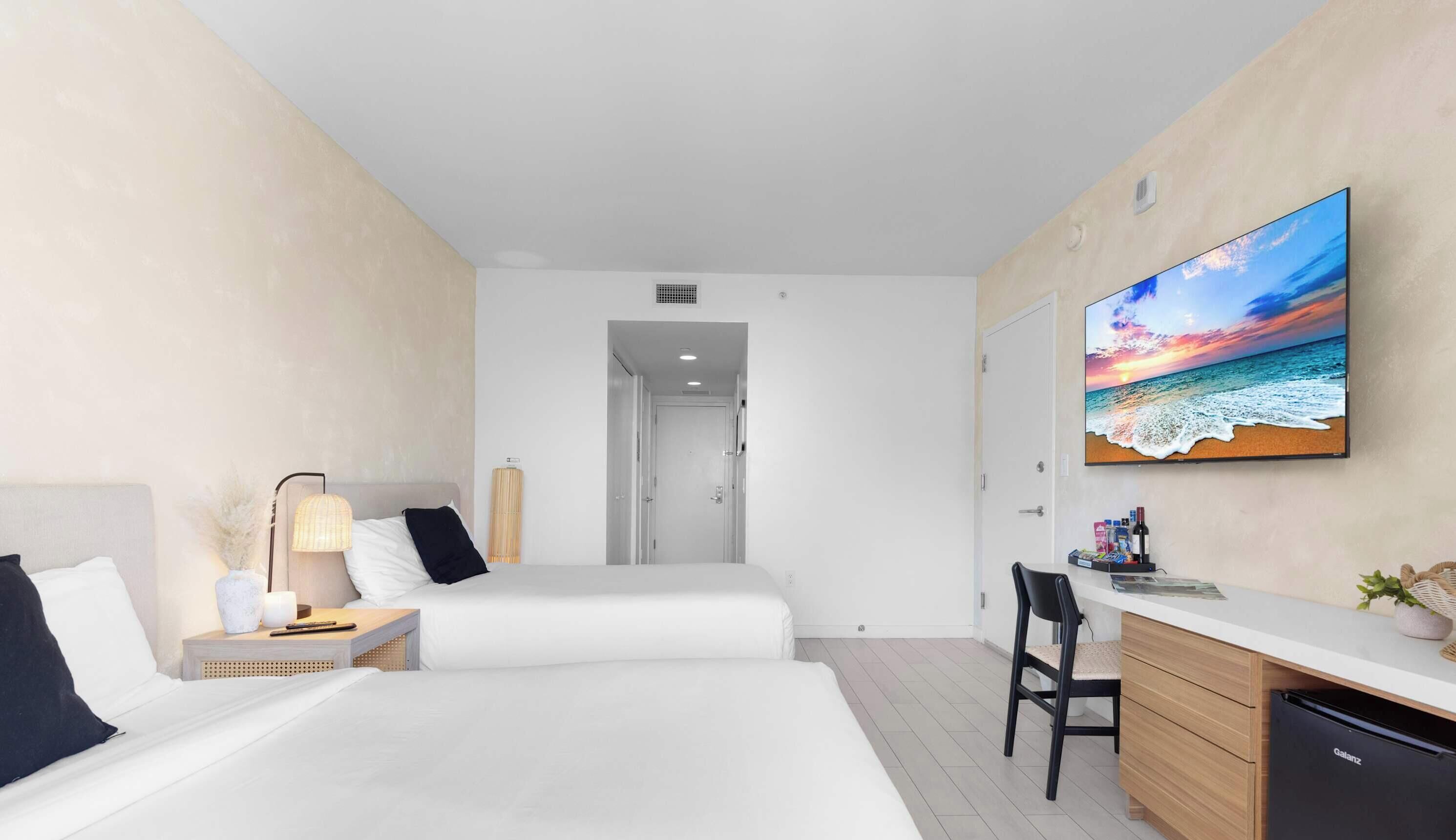 Ein Hotelzimmer mit zwei Betten, einem Schreibtisch, einem Stuhl und einem großen Gemälde mit Strandansicht.