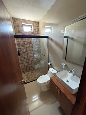 Et badeværelse med bruseniche, toilet, vask og spejl.