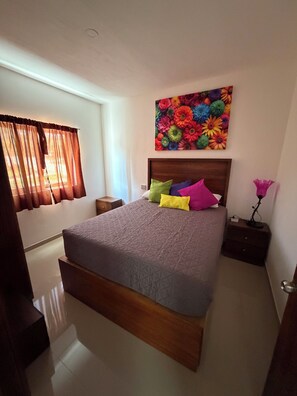 Un dormitorio con cama, mesita de noche, lámpara y un cuadro con motivos florales en la pared.