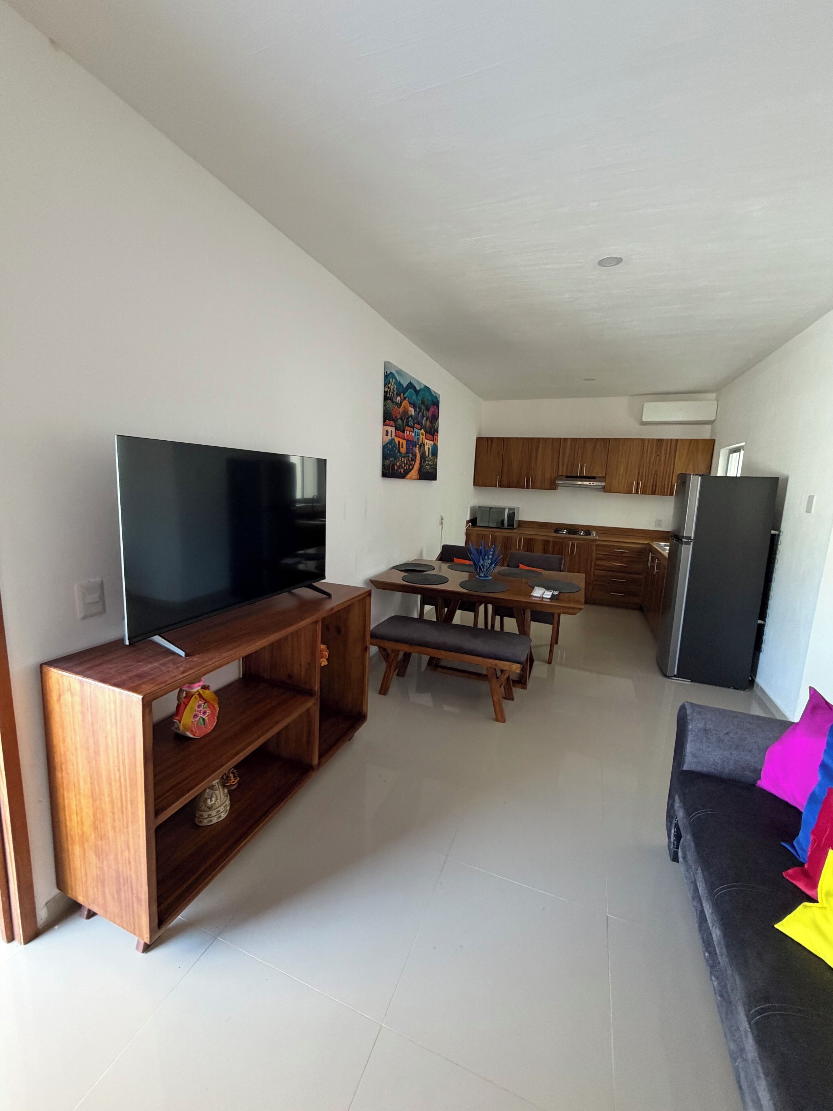 A modern living room with a flat-screen TV, wooden entertainment unit, and a sofa with colorful cushions.