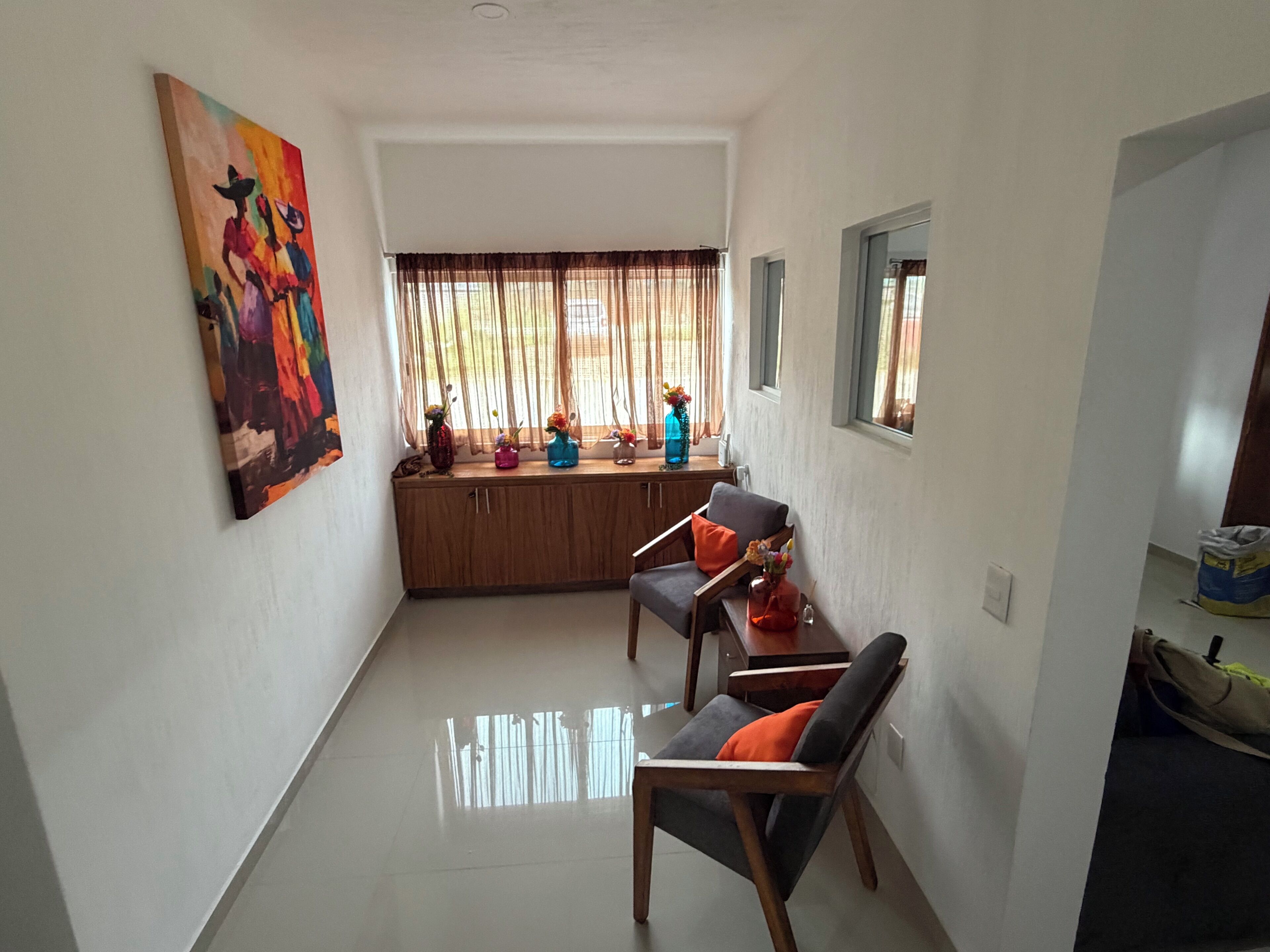 A compact living space with a kitchenette, a dining area with a sofa and chairs, and a large window with curtains.