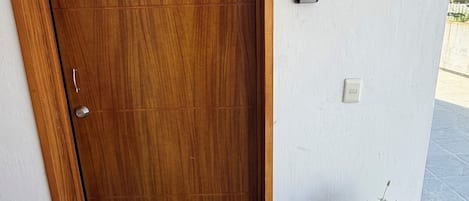 Eine Holztür mit einem 'B'-Schild, einem Blumentopf und einer Fußmatte.