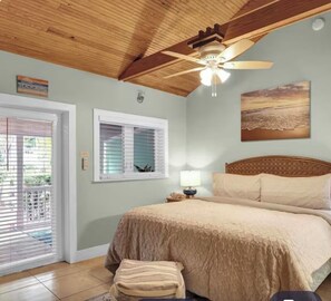 A bedroom with a bed, a ceiling fan, a window with blinds, and a painting on the wall. - Coconut Mallory~ Cozy Studio bungalow in tranquil Key West with AC (Key West)