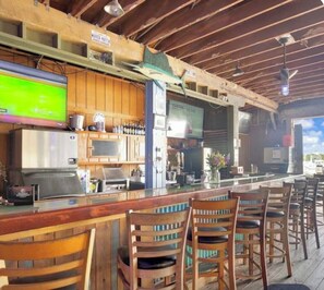 A bar area with wooden chairs, a counter, and a television screen. - Coconut Mallory~ Cozy Studio bungalow in tranquil Key West with AC (Key West)