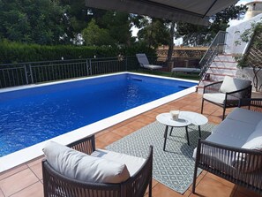 Piscina rectangular con borde de azulejos, rodeada por un patio con mobiliario exterior, incluyendo sillas y una mesa.