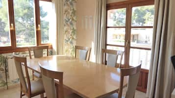 Un coin repas avec une table ronde et des chaises, de grandes fenêtres avec des rideaux et une vue sur l’extérieur.
