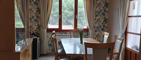 Ein Essbereich mit Tisch und Stühlen, einem Fenster mit Vorhängen und einer Heizung.
