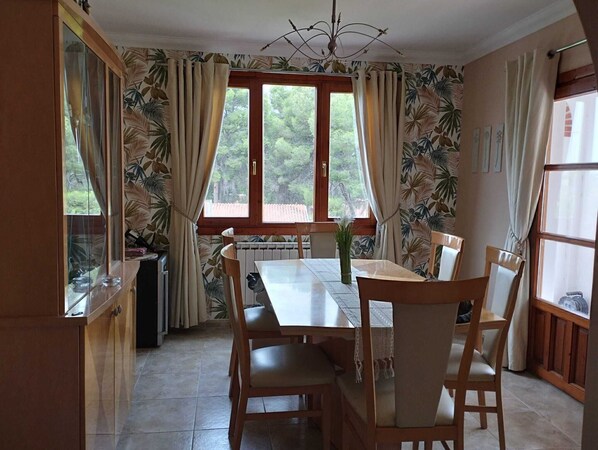 Un coin repas avec une table et des chaises, une fenêtre avec des rideaux et un radiateur.