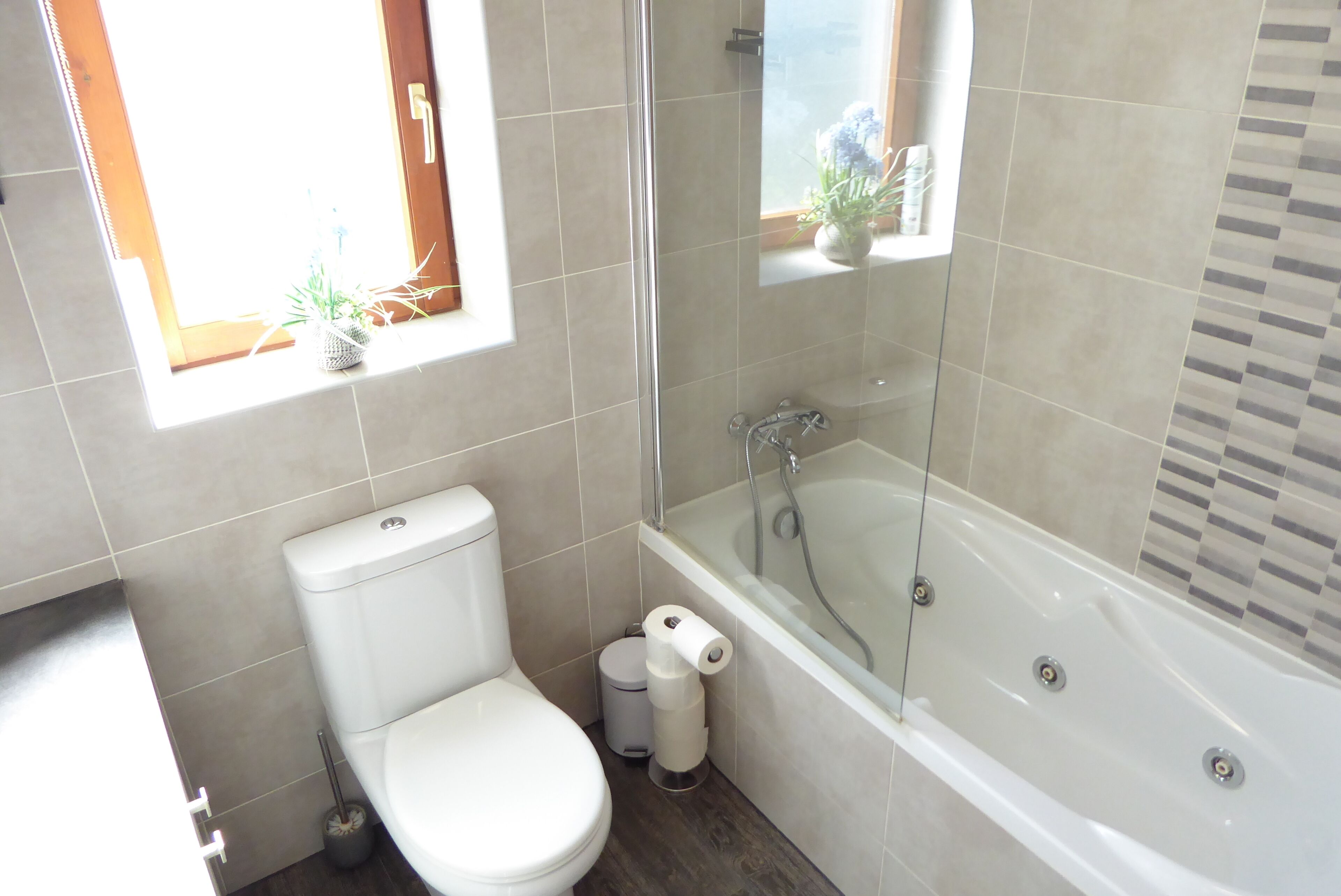 Ein Badezimmer mit Toilette, Bidet, einer Duschkabine und einem Fenster mit Pflanzen.