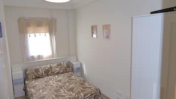 Een slaapkamer met een bed, nachtkastje, kledingkast, raam met gordijnen en twee aan de muur hangende foto's.