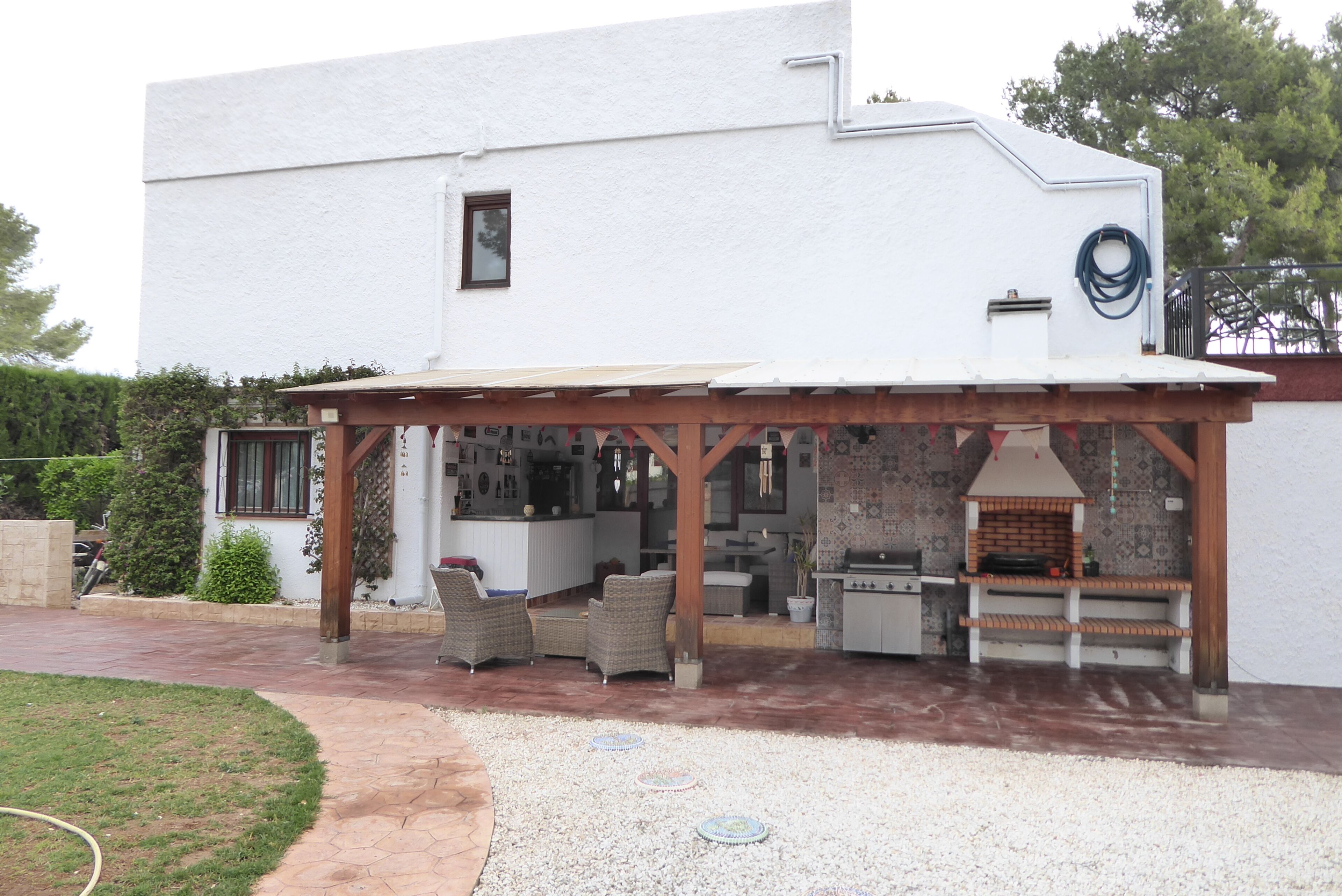 Un bâtiment blanc doté d’un patio couvert, aménagé avec du mobilier d’extérieur et un barbecue.