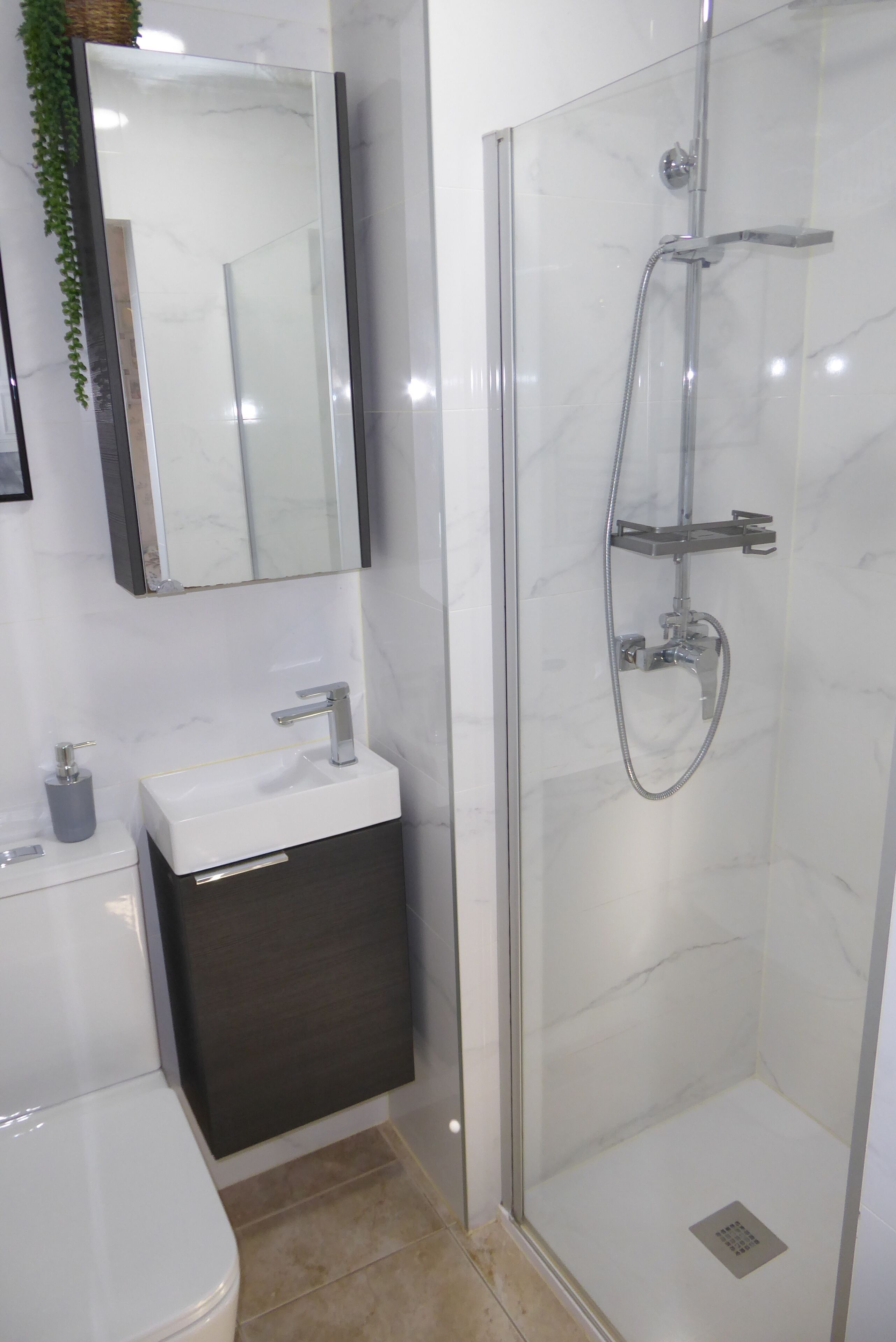 Een moderne badkamer met een douche met glazen wanden, een witte wastafel en een donkere badkamerkast.