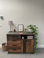 A wooden desk with drawers, a lamp, a framed quote, and a potted plant.