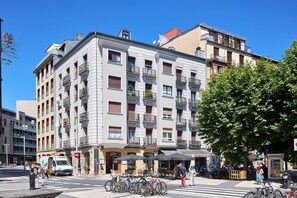 A multi-story building with balconies, a street in front with bicycles and pedestrians, and outdoor seating areas. - Plaza Easo Attic | The Rentals Collection (San Sebastián)