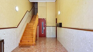 Um corredor com escadas de madeira, uma porta vermelha e um elevador fixado na parede.