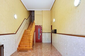 A hallway with a wooden staircase, a red door, and a wall-mounted elevator. - Plaza Easo Attic | The Rentals Collection (San Sebastián)