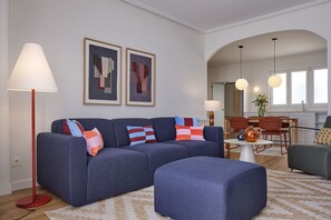 A modern living room with a blue sofa, a red floor lamp, and abstract art on the wall. - Plaza Easo Attic | The Rentals Collection (San Sebastián)