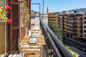 A balcony with a table set for two, overlooking a cityscape with historic buildings and a church spire. - Plaza Easo Attic | The Rentals Collection (San Sebastián)