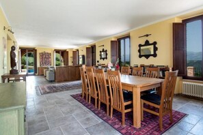 A dining area with a wooden table and chairs, a kitchen in the background, and a view through the window. - Villa Smerillo by MMega (Smerillo)