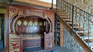 Un letto in legno tradizionale con elaborate incisioni, una scala in pietra e una libreria piena di libri.