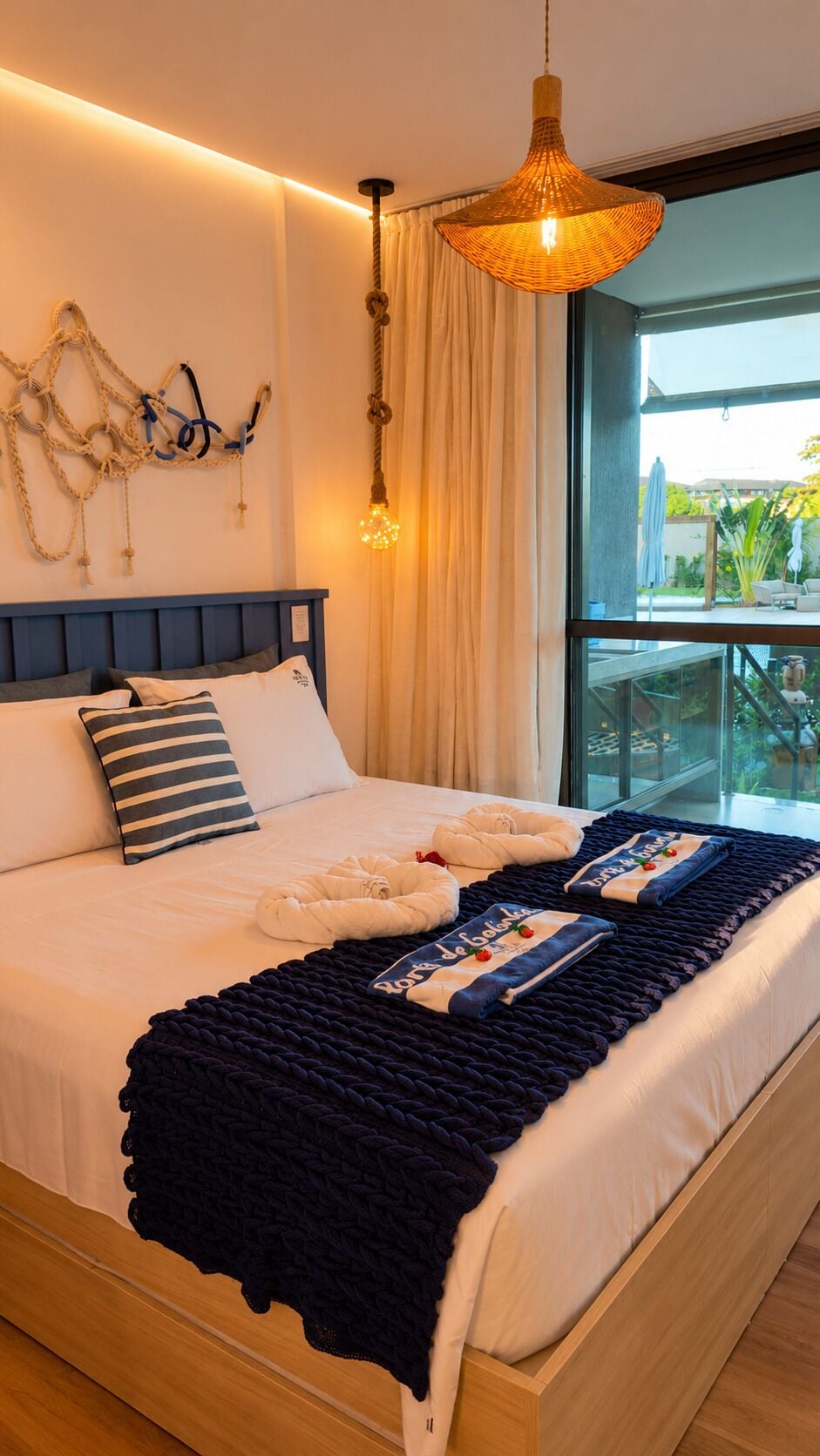 Quarto de hotel com uma cama grande, vista para o exterior e luminária pendente.