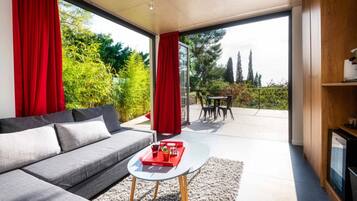 Una sala de estar moderna con un sofá gris, una mesita redonda con bebidas y vistas a un patio con mobiliario exterior.