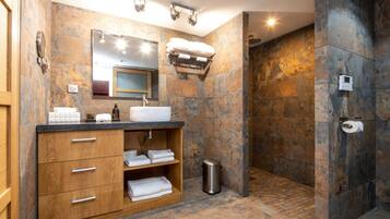 Un baño moderno con pared de piedra, tocador de madera, lavamanos y zona de ducha.