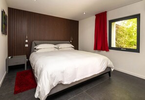 Un dormitorio moderno con una cama grande, una mesita de noche, un tapete rojo y una ventana con vistas al verdor.