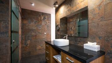 Une salle de bain moderne avec un mur en pierre, un grand miroir, un lavabo blanc et un meuble-lavabo en bois.