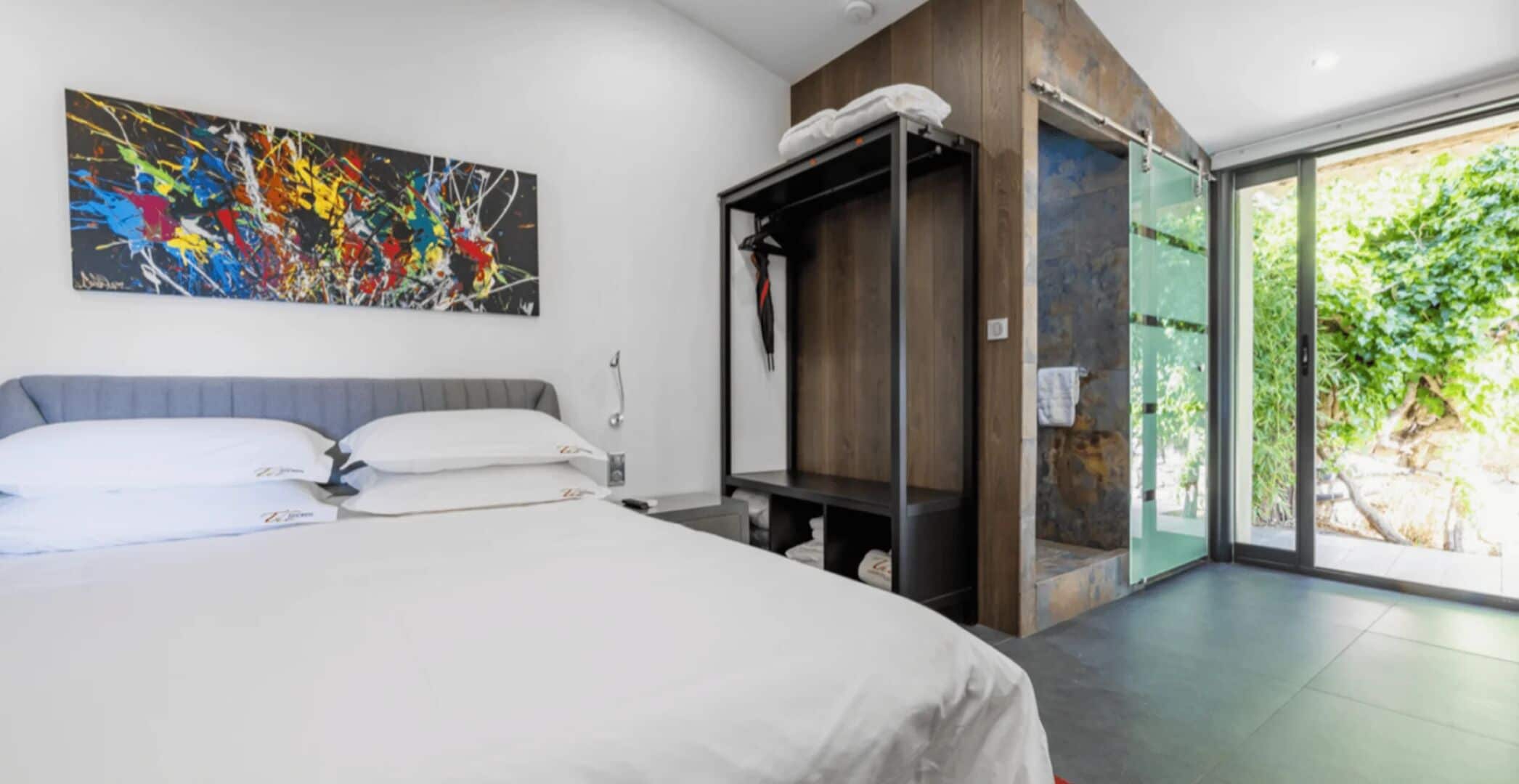 Habitación de hotel moderna con una cama grande, un cuadro en la pared, un armario empotrado y una puerta corrediza de vidrio al exterior.