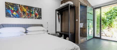 A modern hotel room with a large bed, a painting on the wall, a built-in wardrobe, and a sliding glass door to the outside.