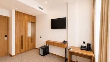 Une chambre d’hôtel avec une armoire en bois, un bureau avec une machine à café, une télévision et un petit réfrigérateur.