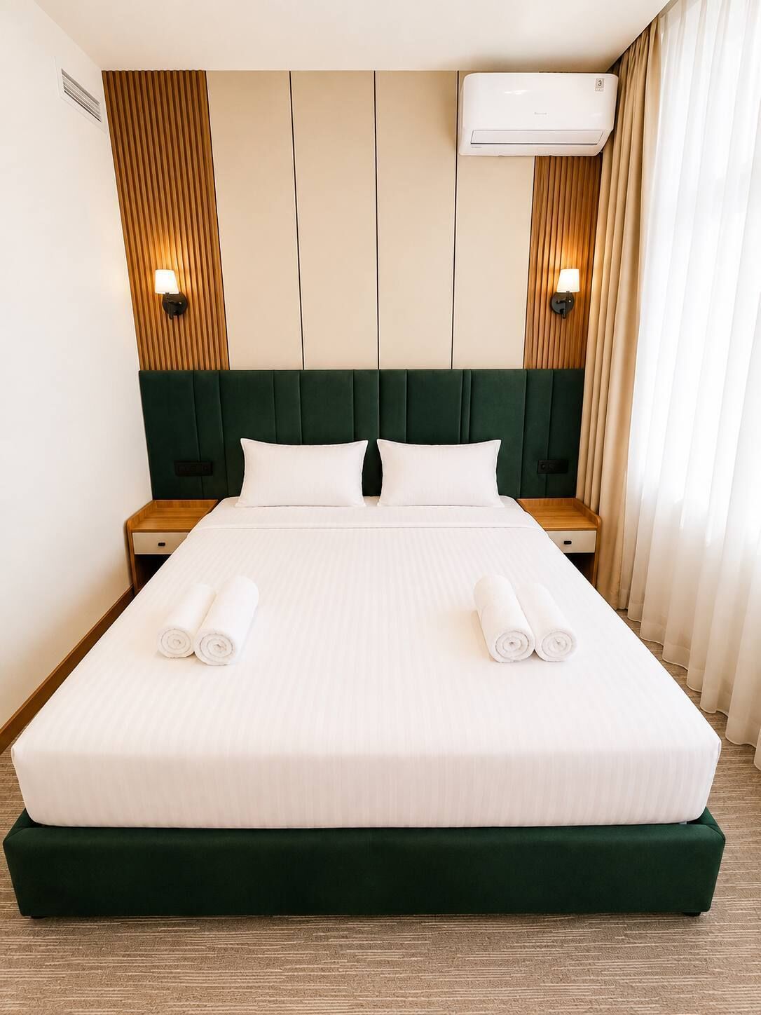 A hotel room with a large bed, two bedside tables, a wall-mounted air conditioner, and a window with curtains.