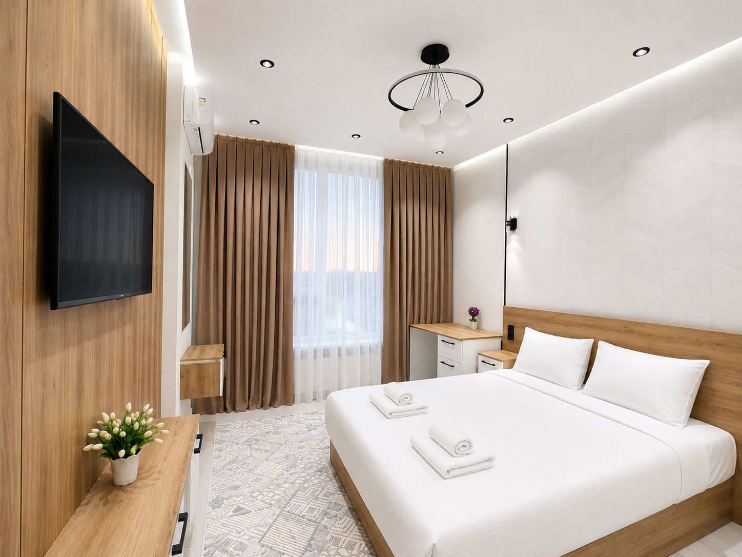 A modern hotel room with a flat-screen TV, a bed with white linens, a wooden headboard, a bedside table with a vase of flowers, and a large window with curtains.