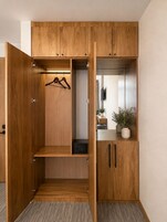 A wooden wardrobe with multiple compartments, a hanging rack, and a small cabinet with a plant.