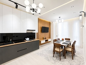 A modern kitchen with a central island, a dining area with a table and chairs, and a TV mounted on a wooden panel wall. - Noor Hotel by Byond (Tashkent)