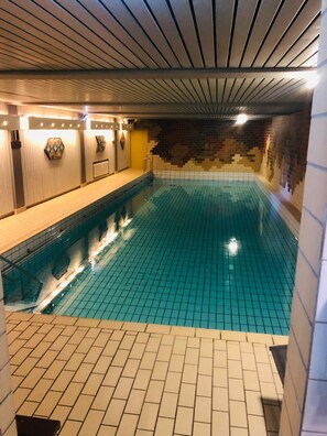 Piscina com piso e paredes revestidas em azulejo, área de deck em madeira e teto com luminárias lineares.