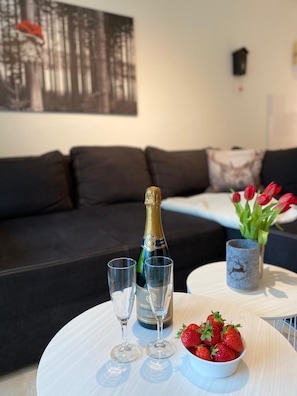 A living room with a black sofa, a white coffee table, a bottle of champagne, two glasses, a bowl of strawberries, and a vase with red tulips. - Kuschelnest Feldberg – Hochschwarzwald Card Included – My SWH (Feldberg)