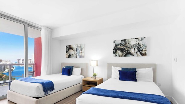 Une chambre d’hôtel avec deux lits, une table de chevet et une vue sur la ville et l’eau.