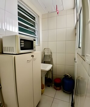 A compact kitchen with a microwave on a cabinet, a sink, and a window with blinds.