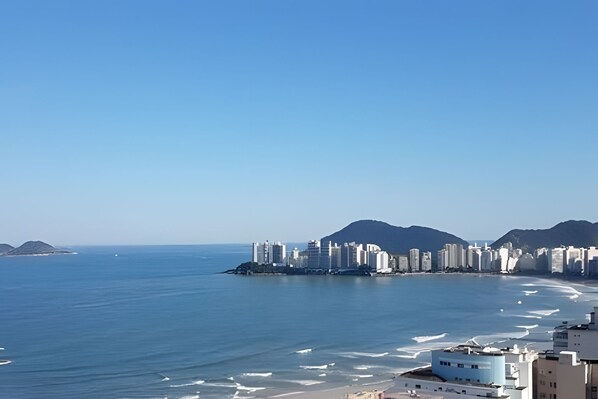 A coastal cityscape with high-rise buildings, a beach, and mountains in the background.