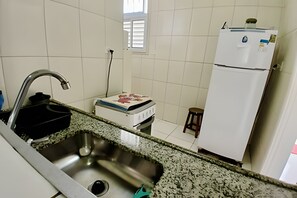 A kitchen with a stainless steel sink, a stove, a white refrigerator, and a window with blinds.