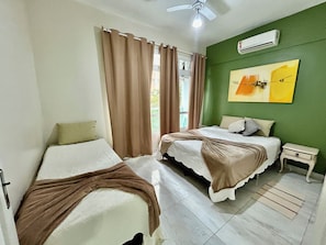 Un dormitorio con dos camas, ventilador de techo, aire acondicionado y una ventana con cortinas.